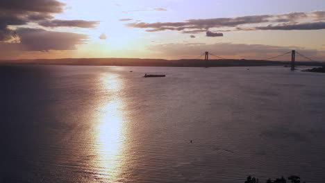 la cámara del dron se desplaza justo sobre el arroyo coney island y observa una puesta de sol dorada y nublada mientras se revela el puente verrazano.