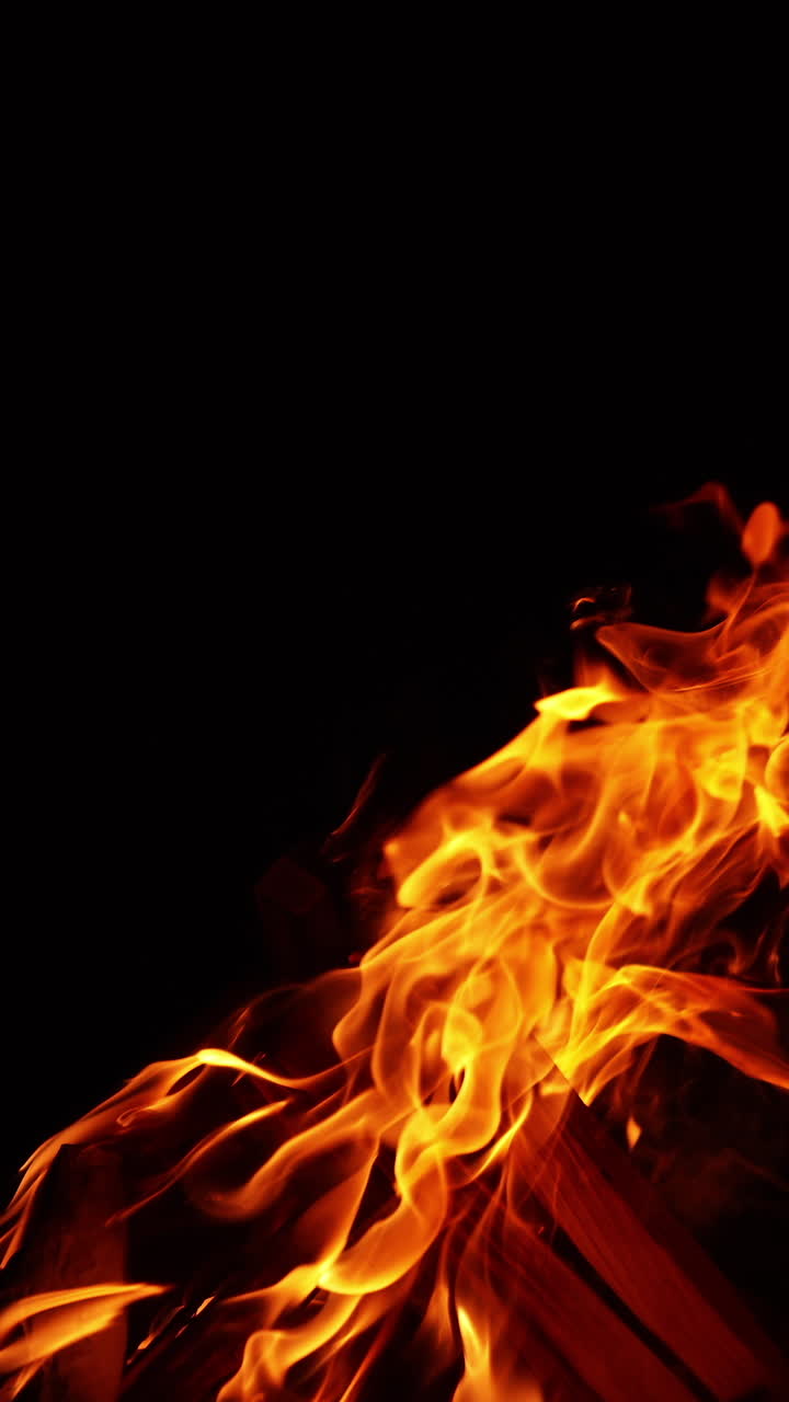 Tronchi di legno accatastati che bruciano con fuoco vivo. Falò spostato a sinistra dal vento. Sfondo nero. Video verticale