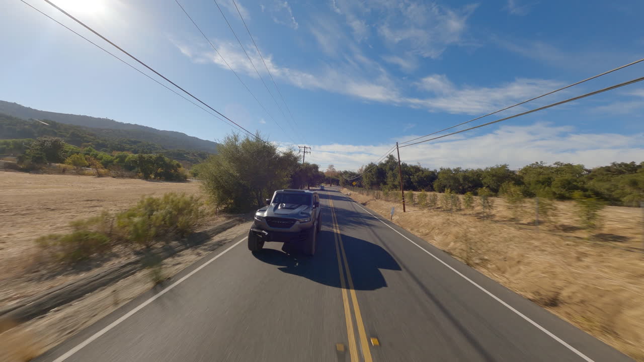 Il Rezvani Tank, la bestia del deserto californiano, ruggisce su strada asfaltata in una giornata di sole, un SUV ripreso frontalmente che insegue una gara di droni FPV ad altissima velocità