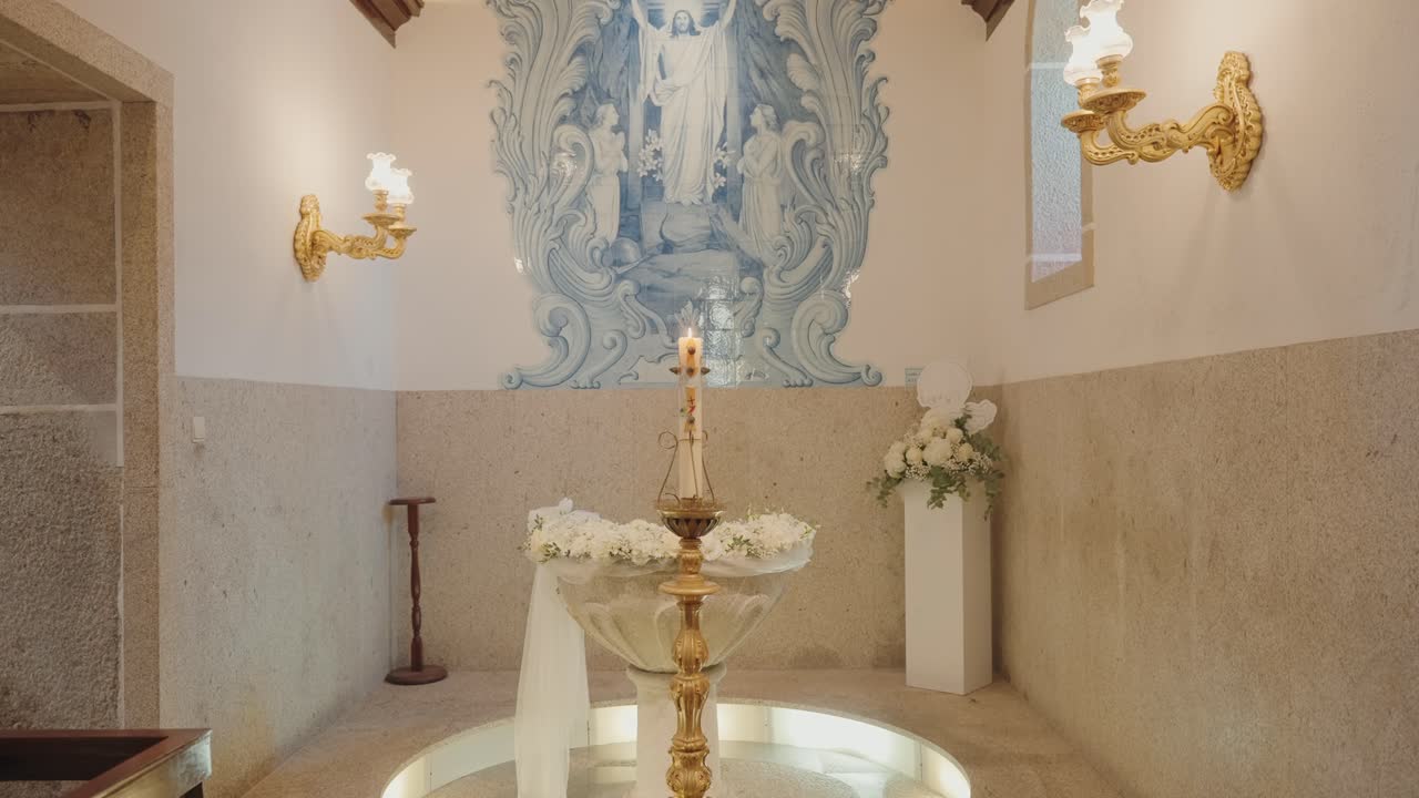 pila bautismal con cirio pascual y decoración floral bajo un mural de azulejos azules en una iglesia