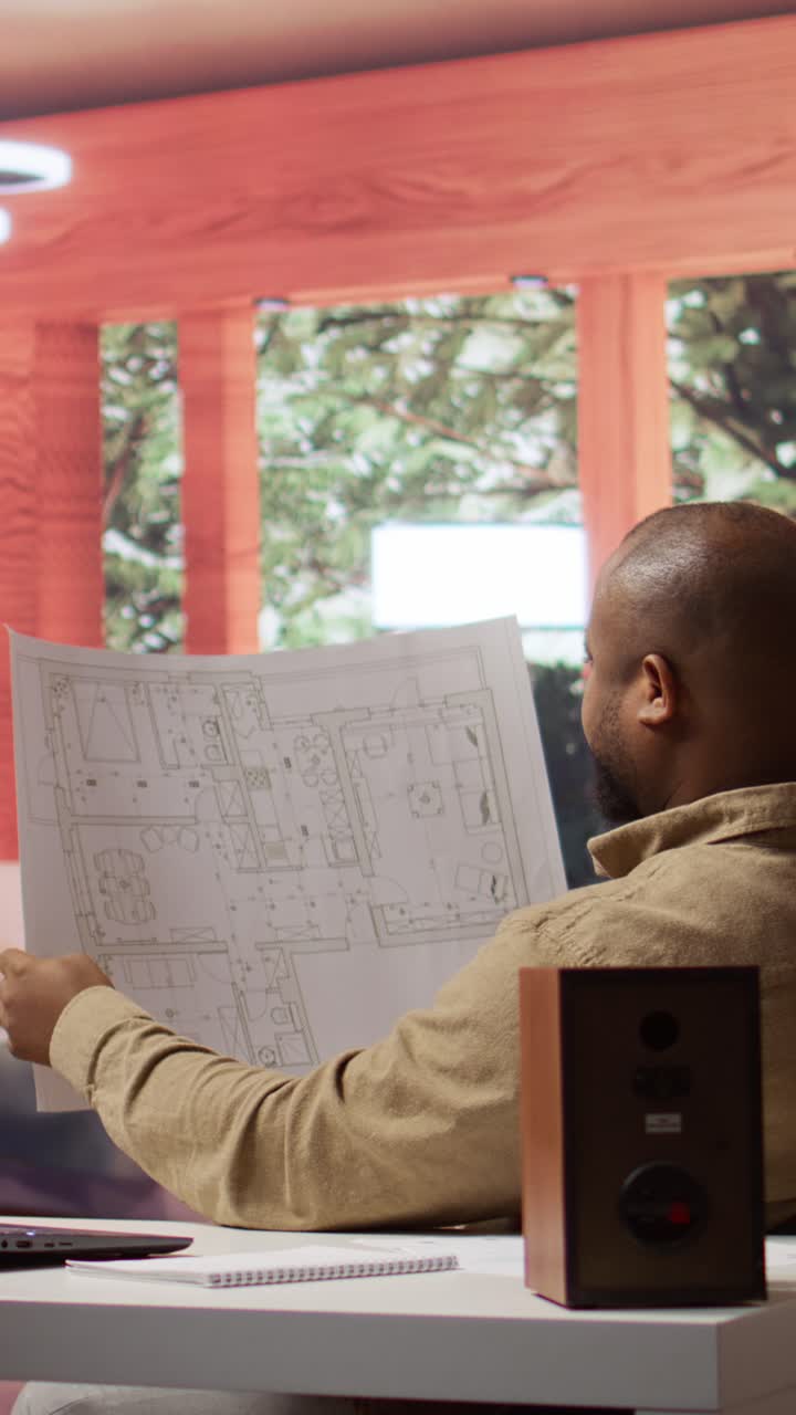 African American Man Examining Architectural Blueprints in Office
