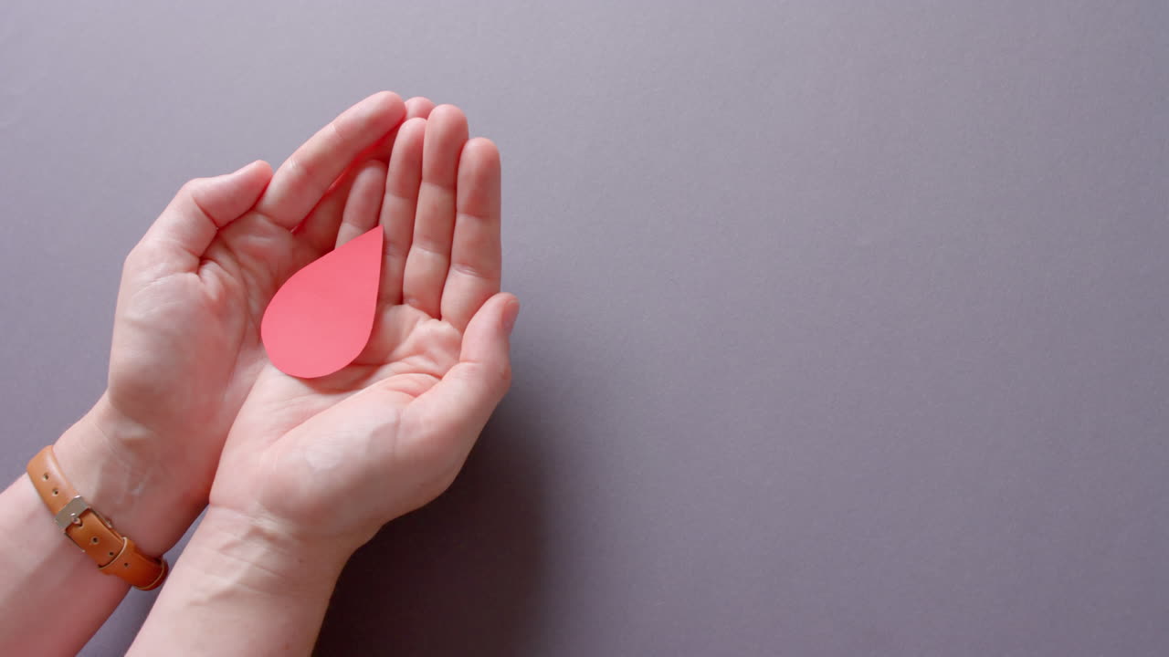 las manos de una mujer caucásica tomando gotas de sangre en un fondo gris con espacio de copia, cámara lenta.