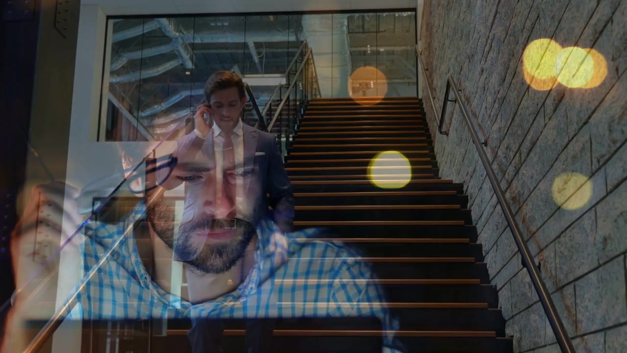 Uomo d'affari al telefono che scende le scale, con un collega sovrapposto che si sistema gli occhiali, effetto bokeh.
