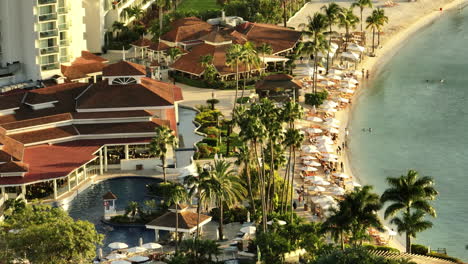 Luxury-resort-aerial-pan-of-the-beach-and-pool,-while-the-sunsets-over-the-Jamaican-ocean