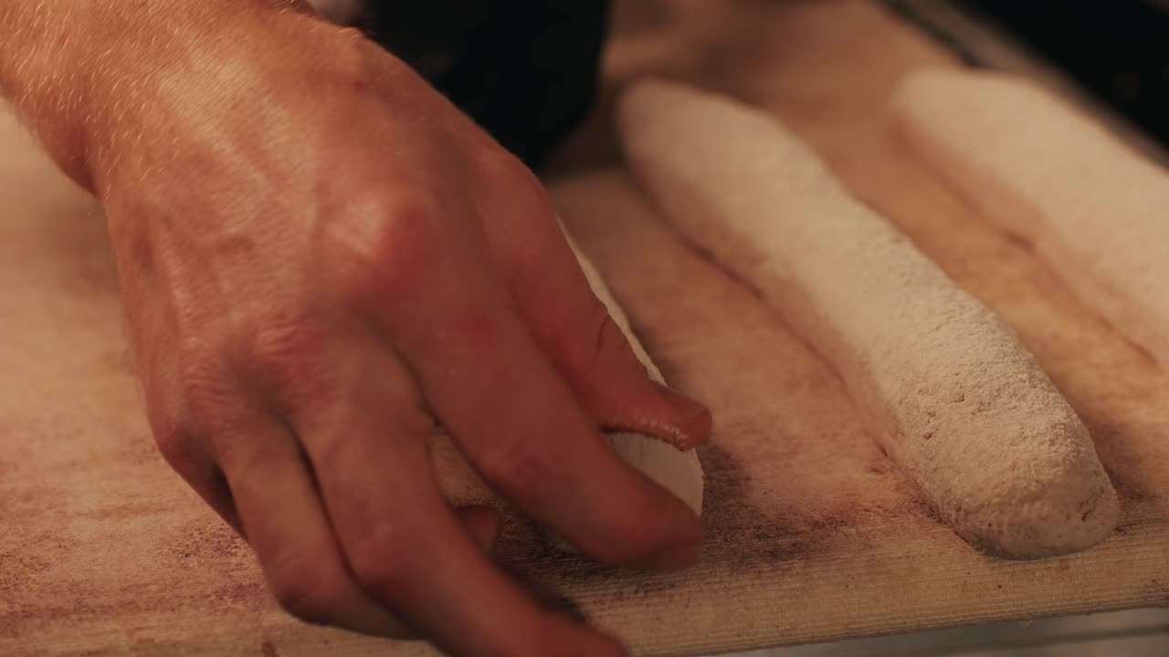 Bakery chef making fresh Artesian buns and baguettes using traditional recipe close-up. Young man kneading dough. Artisan bread is making by skill bakers using natural and high-quality ingredients. Food with health and flavour benefits. Bakery shop and market