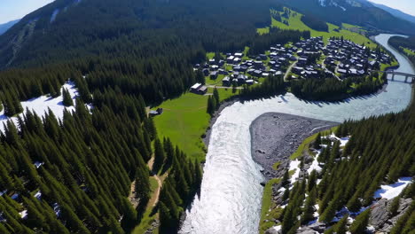 aerial view of a mountain river winding through a forested valley with a village