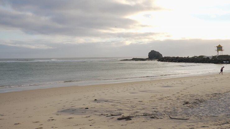 Mer calme à la plage de Currumbin au lever du soleil - Le rocher de Currumbin avec tour de sauveteur au loin - Currumbin Alley, Gold Coast, Queensland, Australie - plan large