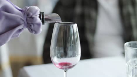 primer plano desconocido camarero mano vertiendo vino en vaso en el interior. mujer joven mano tomando vaso de vino con bebida en el interior del restaurante.