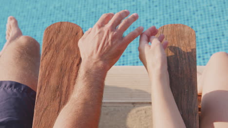 primer plano de una pareja cogida de las manos en las vacaciones de verano tomando el sol en tumbonas junto a una piscina al aire libre