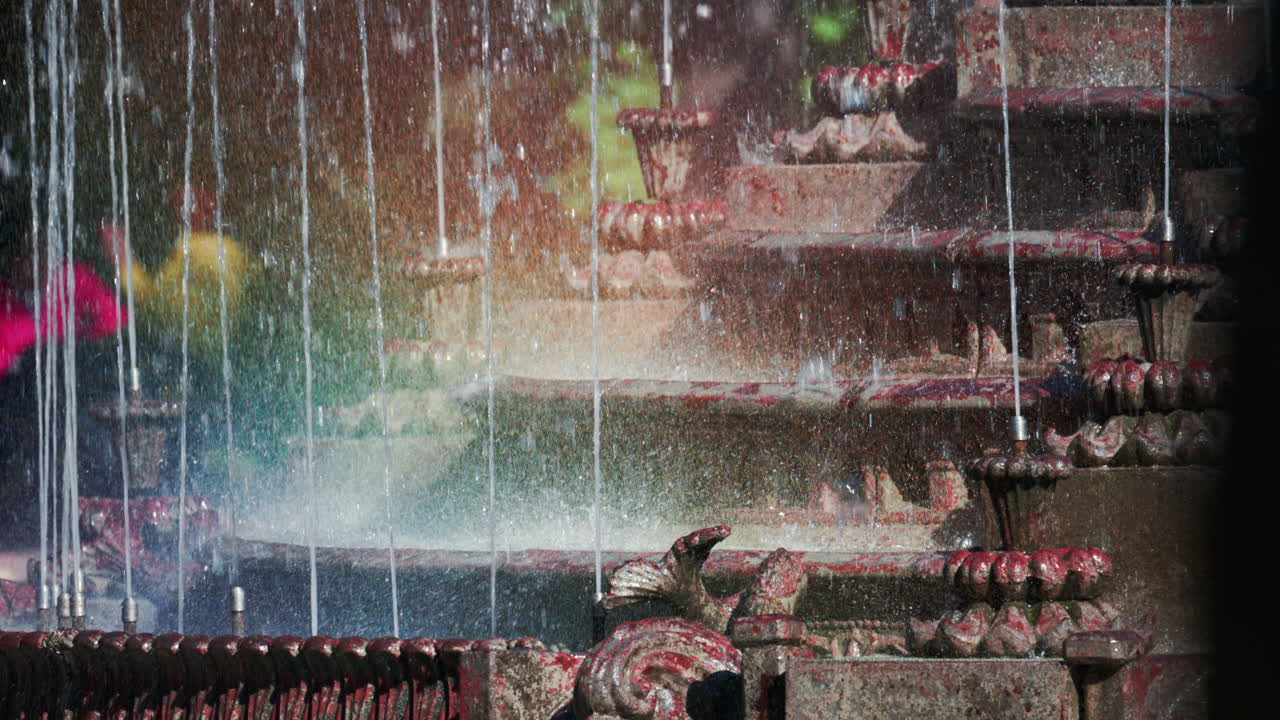 View of a decorative fountain with sparkling water droplets illuminated by sunlight in a park