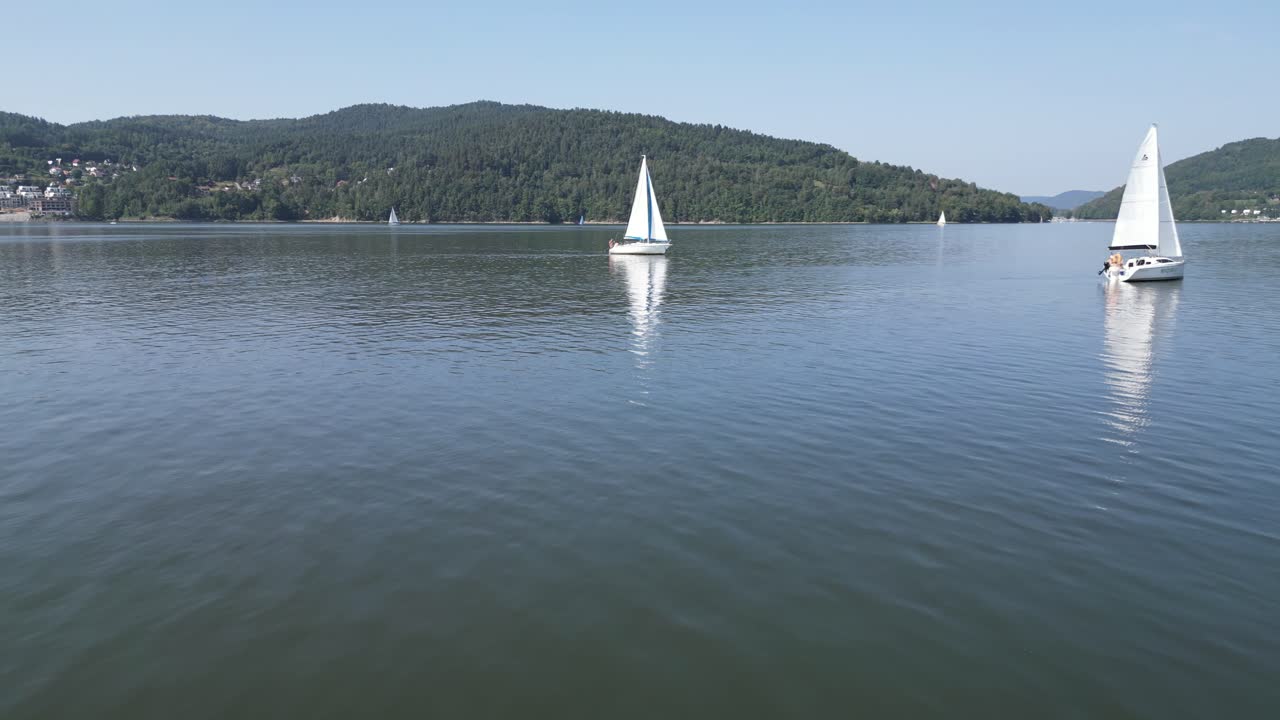barcos de vela blancos en el lago tranquilo en las montañas beskid, rodeados de vegetación durante un día de verano - vista aérea 4k