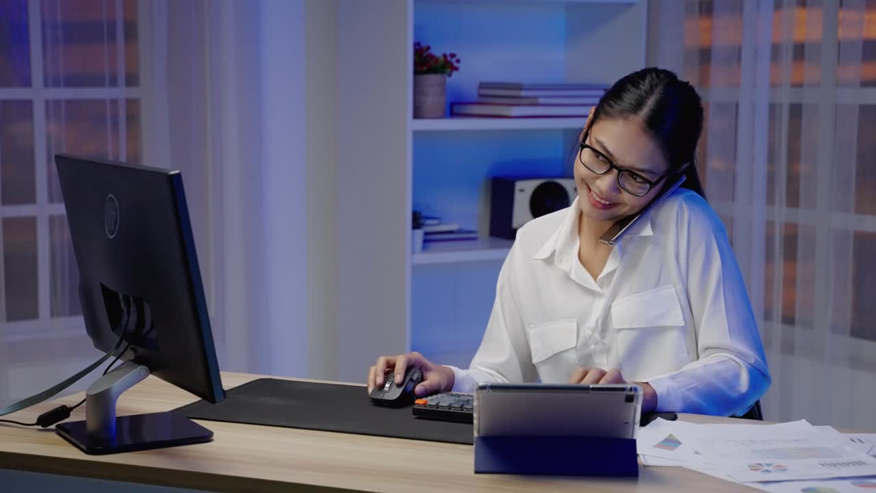 una mujer de negocios asiática o independiente está ocupada en el trabajo, habla por teléfono y escribe hasta horas extras por la noche.