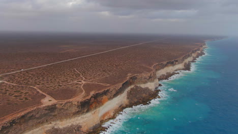 aerial view showing van on empty road above gigantic cliffs and ocean during cloudy day - nullarbor sa, australia