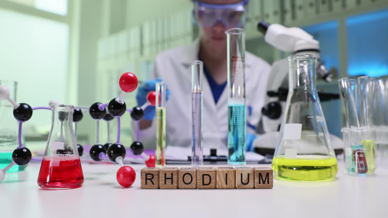 A scientist conducting experiments in a chemistry laboratory with various equipment and a molecular model spelling 'RHODIUM'