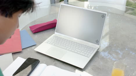 A-young-Asian-male-college-student-sitting-at-table,-focusing-on-a-laptop-screen