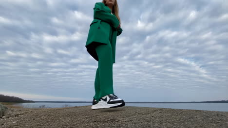 person in green suit and sneakers by the water under a cloudy sky
