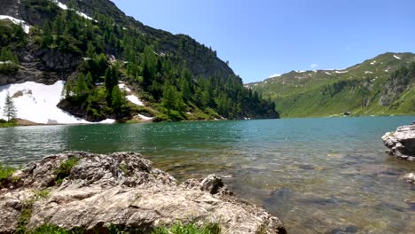 Toma-Panorámica-Del-Idílico-Río-De-Montaña-Rodeado-De-Montañas-Verdes-Y-Nieve-En-La-Orilla-Del-Río---Cambio-Climático-Y-Calentamiento-Global