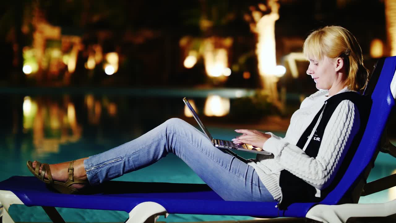 una mujer joven usa una computadora portátil junto a la piscina