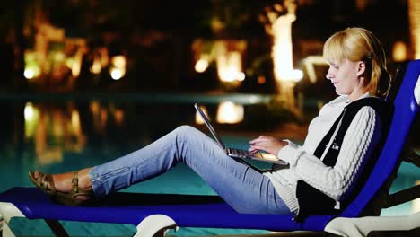 a young woman uses a laptop at poolside