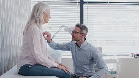 médico escuchando a una paciente femenina madura respirando con estetoscopio durante un examen médico en la oficina