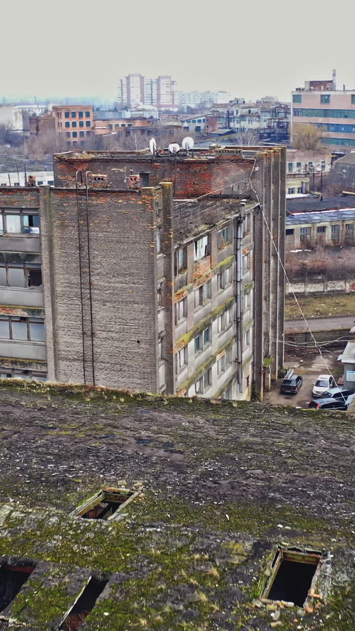 Almost destroyed building with holey roof in the city. Top view of ruined industrial building and some cars on a road. Aerial view Vertical video