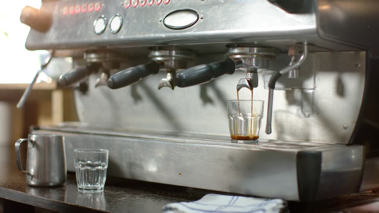 Una mano posiziona un bicchierino da shot mentre una macchina eroga un doppio caffè per riempire il bicchierino al bancone.