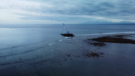 aerial view of an impressive shipwreck with blue crane stranded on the rocky beach shore of the popular tourist destination nusa lembogan in bali, indonesia during a sightseeing trip on vacation