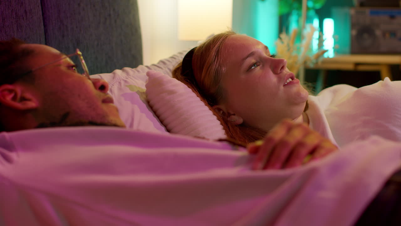 una pareja riendo en la cama mientras ven la televisión por la noche