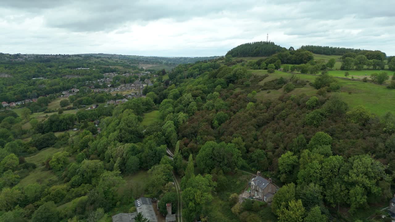 Drone aerial view of Bolehill mountain, hiking path, and green forests in rolling countryside Derbyshire Dales England UK
