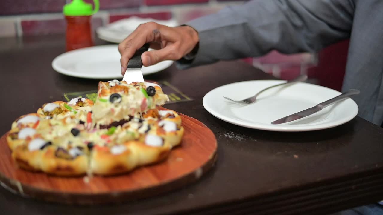 Young man is bringing piece of pizza from plate to face