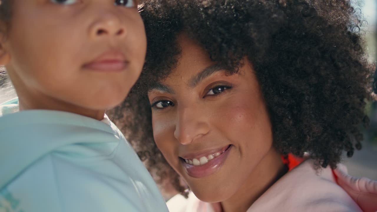 Mãe e filha olhando para a câmera sorrindo ao ar livre em close-up. Retrato de família