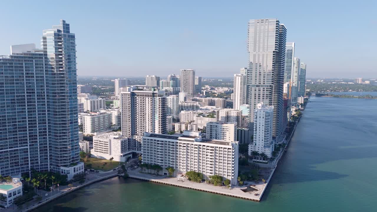 Aerial drone view of downtown Miami’s waterfront skyline, featuring modern high-rise buildings, luxury yachts, and turquoise Biscayne Bay under a clear blue sky.