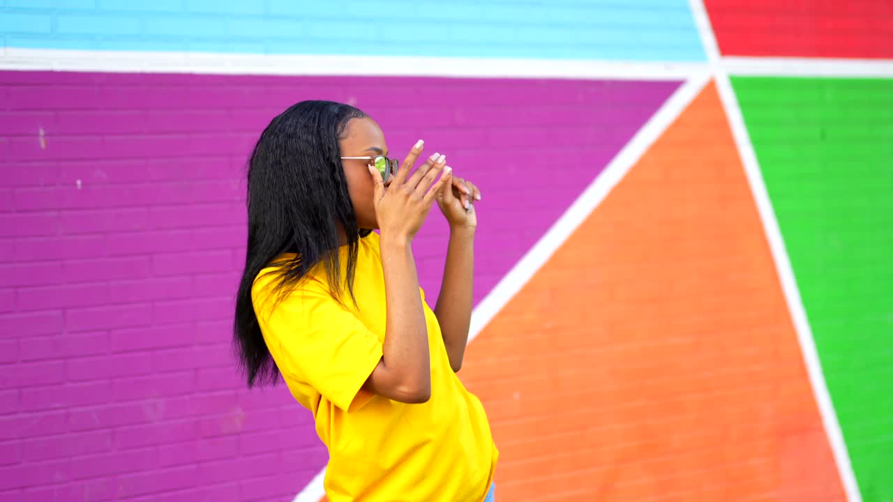 Woman in yellow shirt and sunglasses in front of colorful wall