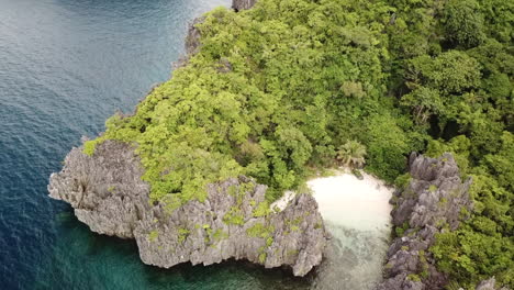 amazing white sandy isolated beach between green trees on a rocky island with bright water slowly rooling on a sunny day. drone dolly shot