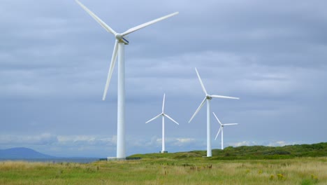 windmills on coastline with mountains in distance on cloudy bright summer day