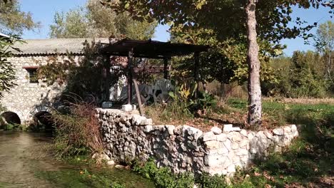 Panning-from-a-Small-rolling-creek-to-a-stone-house-on-a-sunny-day-in-nature-in-Northern-Greece,-Kefalari,-Drama