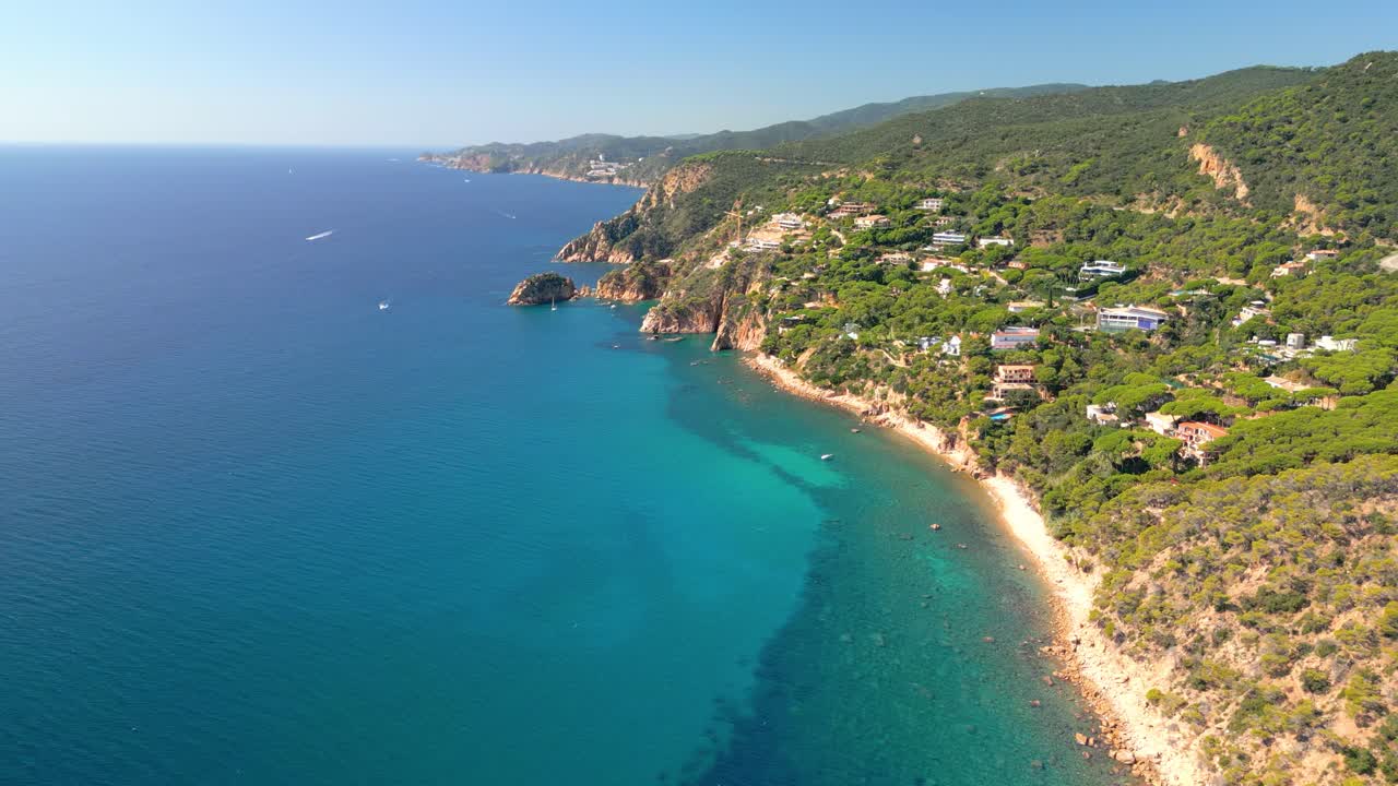 Beautiful aerial view flying over the mediterranean coast of sant feliu de guixols in costa brava, spain, with turquoise clear water, rugged cliffs, and lush green hills on a sunny day