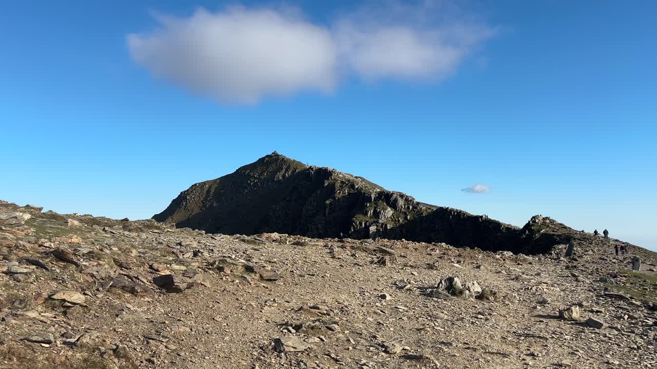 Wide scenic view of peaceful mountain ridge captured from high open ground in Snowdonia National Park with sunlight casting soft shadows over rugged terrain under bright clear sky