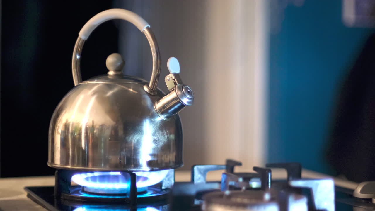 Shiny stainless steel kettle boiling on gas stove starting to whistle and steam