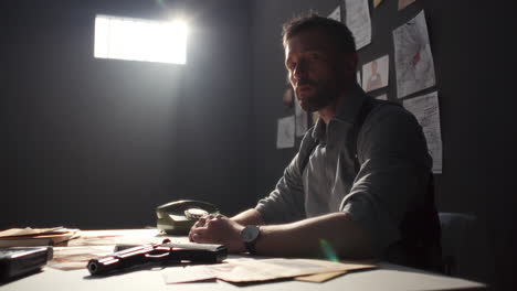 portrait of serious detective sitting at table in interrogation room