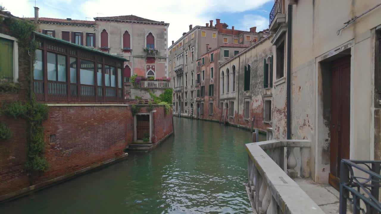 A slow-motion view of a Venice canal in Italy, featuring brick buildings and a serene waterway with a small balcony