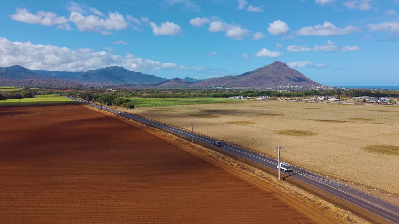 Aerial view of Mauritius countryside with vibrant red soil fields, golden farmlands, and a scenic mountain backdrop under clear blue skies. Concept of agriculture, rural beauty, and natural harmony