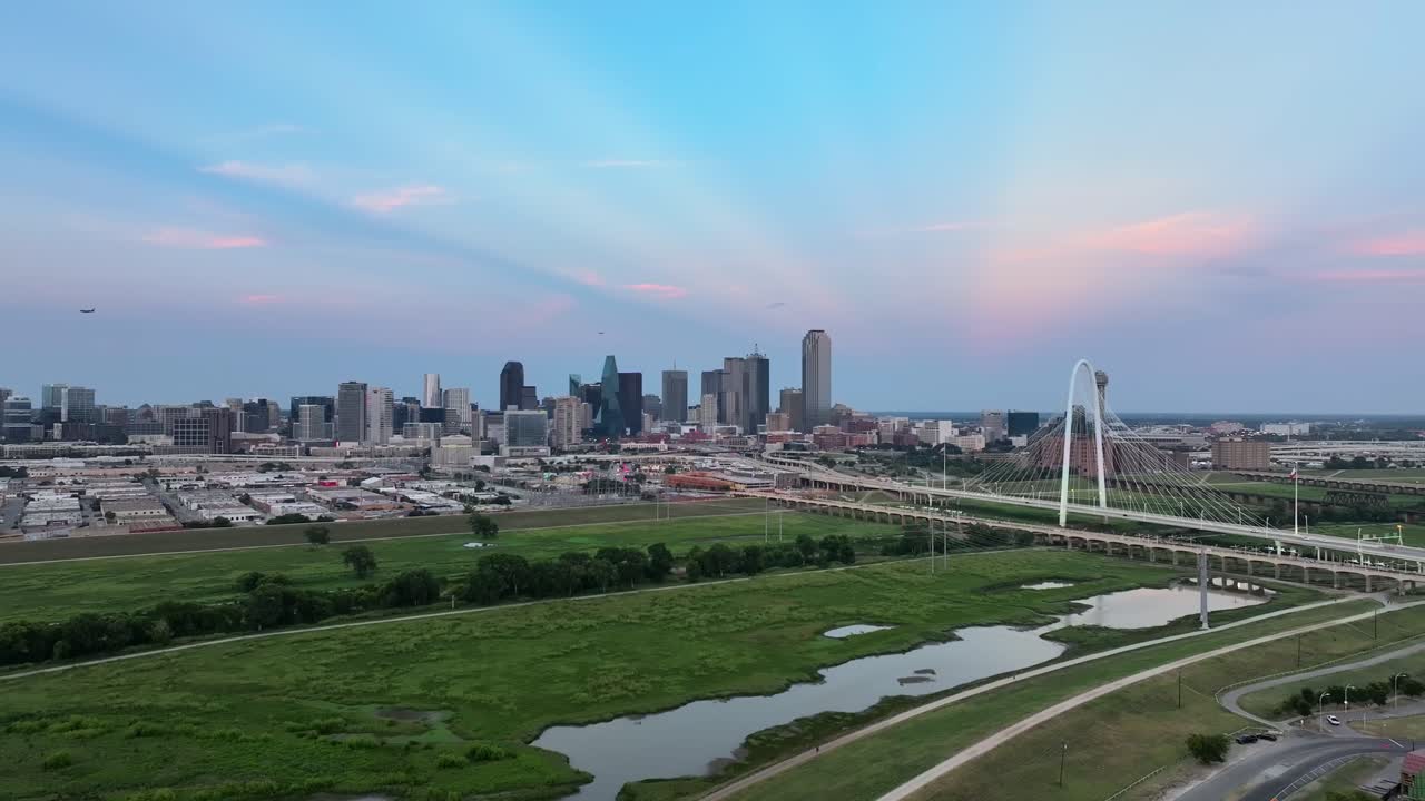 Wide aerial of Dallas, Texas skyline with bridge and busy highway; daytime, clear skies. Urban architecture and transportation in one sweeping drone shot