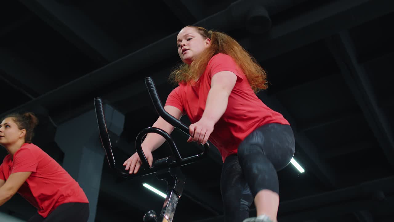 Group of smiling friends women class exercising, training, spin on stationary bike at modern gym