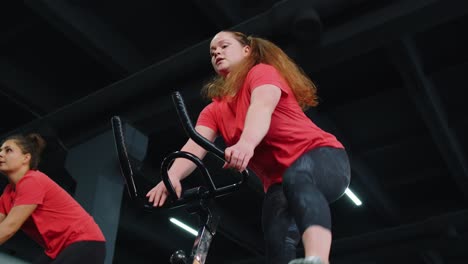 Group-of-smiling-friends-women-class-exercising,-training,-spin-on-stationary-bike-at-modern-gym