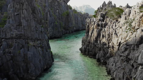 tiro de drones pasando entre grandes rocas de basalto que revelan una playa escondida en el nido, palawan