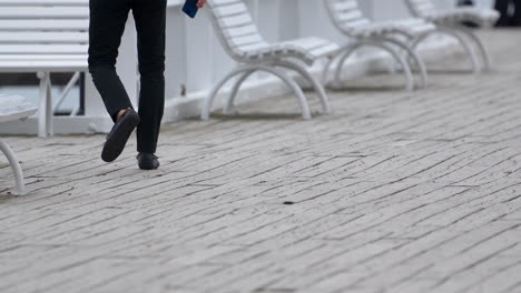 Un-Hombre-Con-Pantalones-Negros-Caminando-A-Cámara-Lenta-Por-El-Muelle-Sosteniendo-Un-Teléfono-En-La-Mano