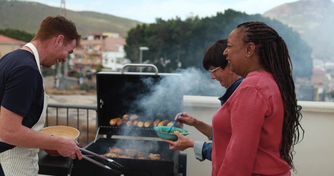 Amici multietnici felici che ridono mentre cucinano al barbecue sul tetto
