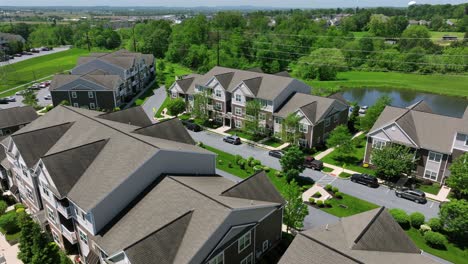 aerial view of american suburban architecture with modern townhouses with symmetrical designs, gabled roofs and large windows. sunny day with pond and green trees in background. suburb district of usa