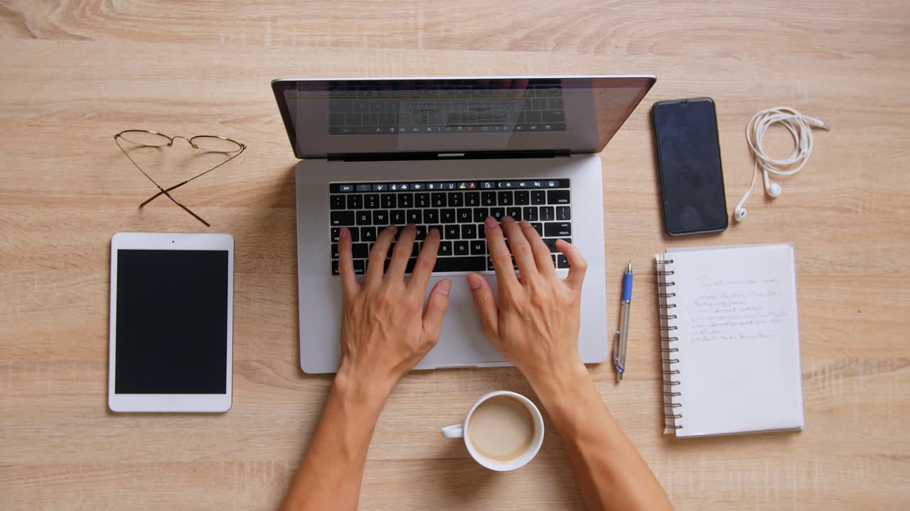 Person working at a desk with laptop, tablet, and other office supplies.